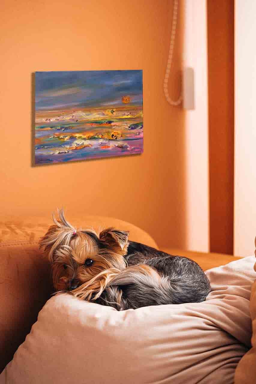 Photo of cute puppy sleeping in bed on a pillow, having the painting on the wall in the background, predominantly orange in the painting and its surroundings